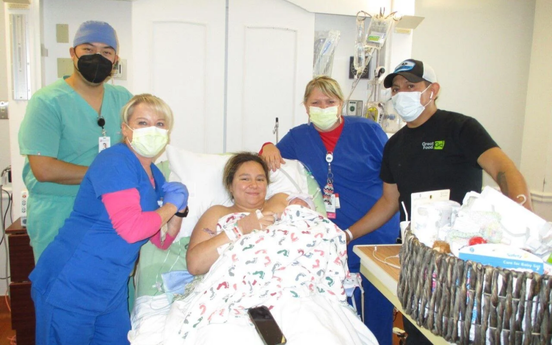 Staff members and parents standing around a hospital bed with a mother holding a baby.